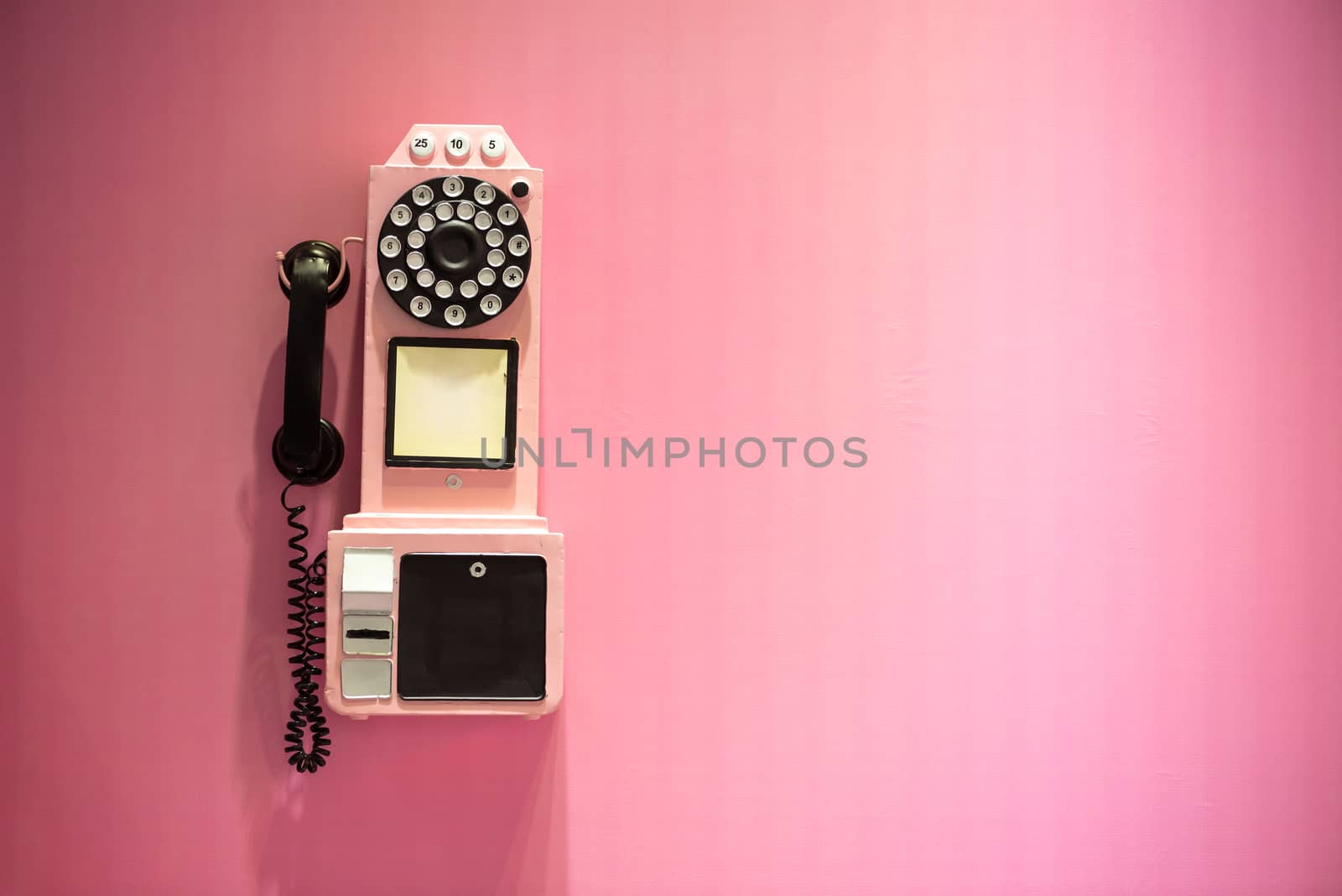 Old vintage phone hanging on a pink wall with copy space