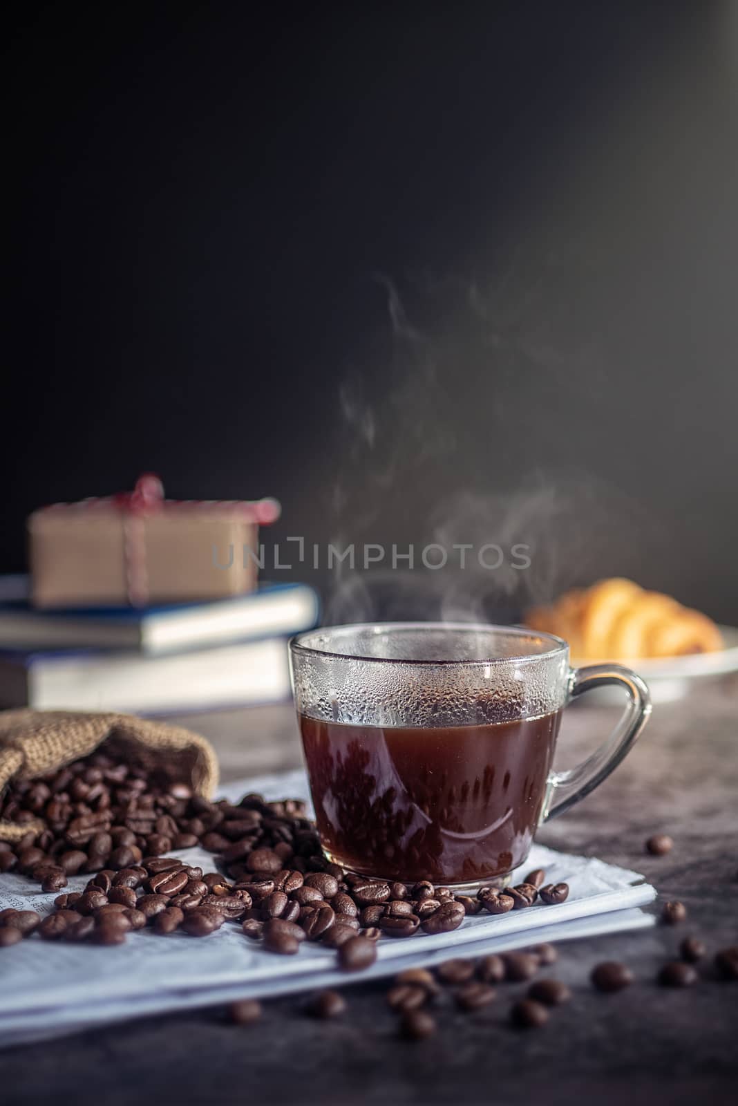 a cup of hot espresso coffee drink with smoke and roasted coffee beans on the table in the morning. vertical image, cropped shot by asiandelight