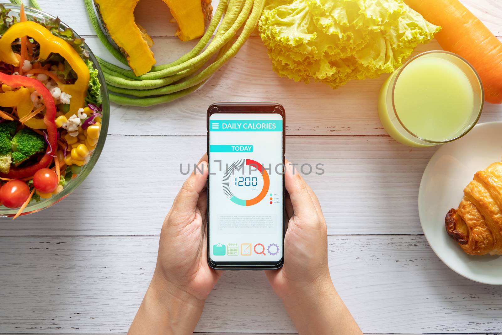 Calories counting and food control concept. woman using Calorie counter application on her smartphone with salad , vegetable, juice and croissant on dining table by asiandelight