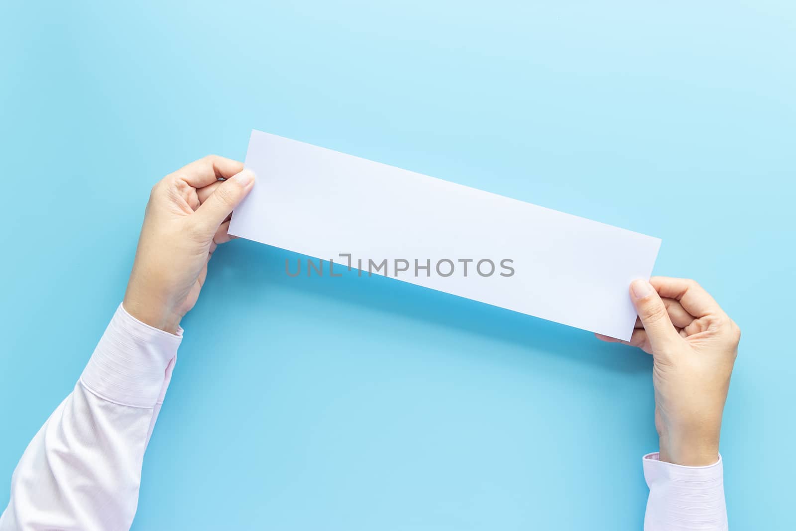 close up hands holding empty white blank horizontal paper for flyer or invitation mock up isolated on a blue background.