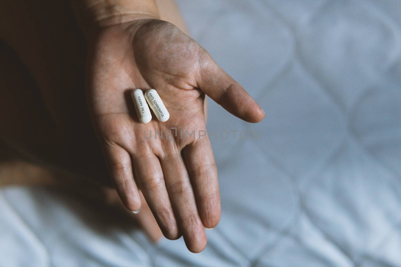 Two white capsules in a woman's hand while sitting on the bed. Happy pill capsule, Anti sorrowful capsule.