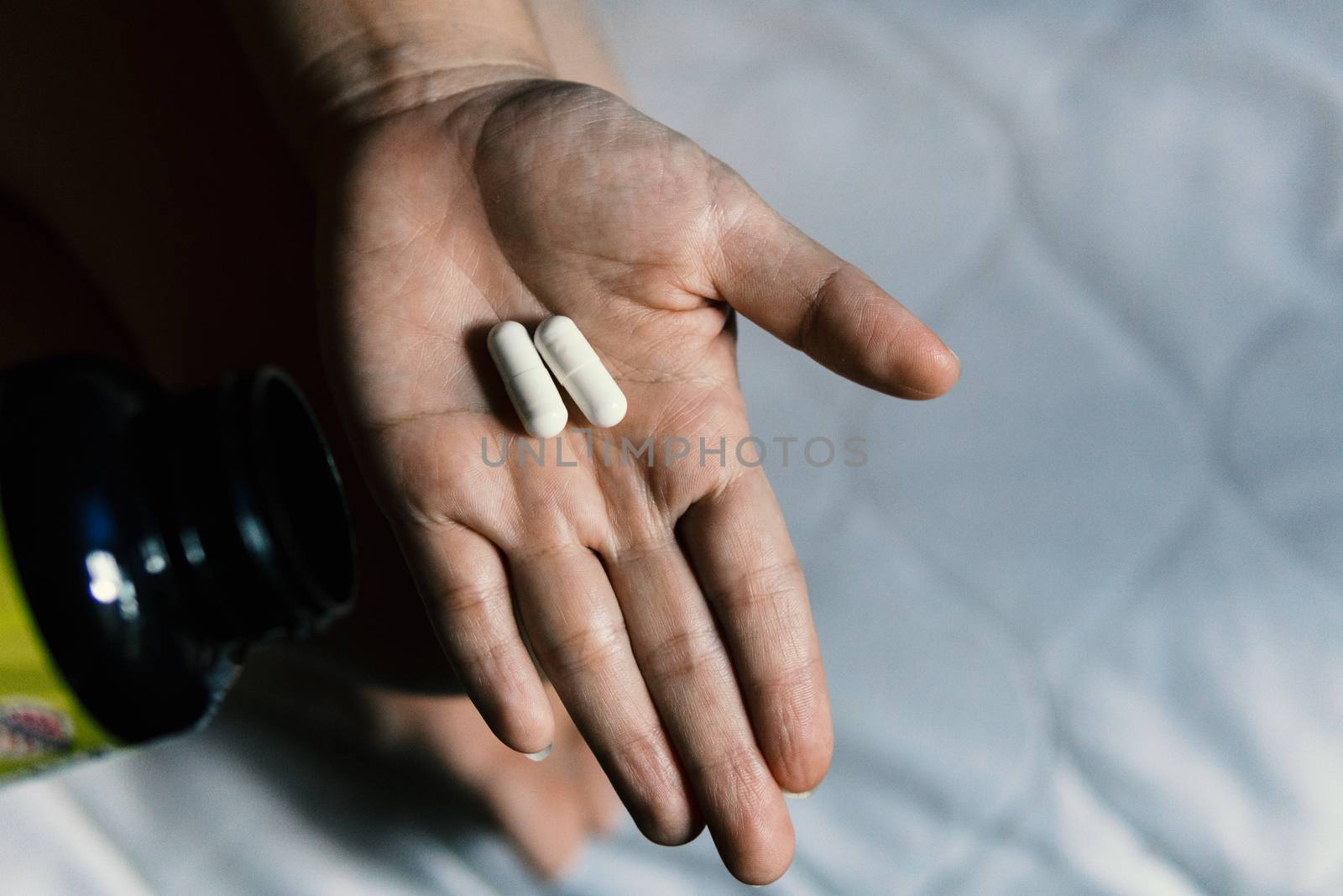 Two white capsules in a woman's hand while sitting on the bed