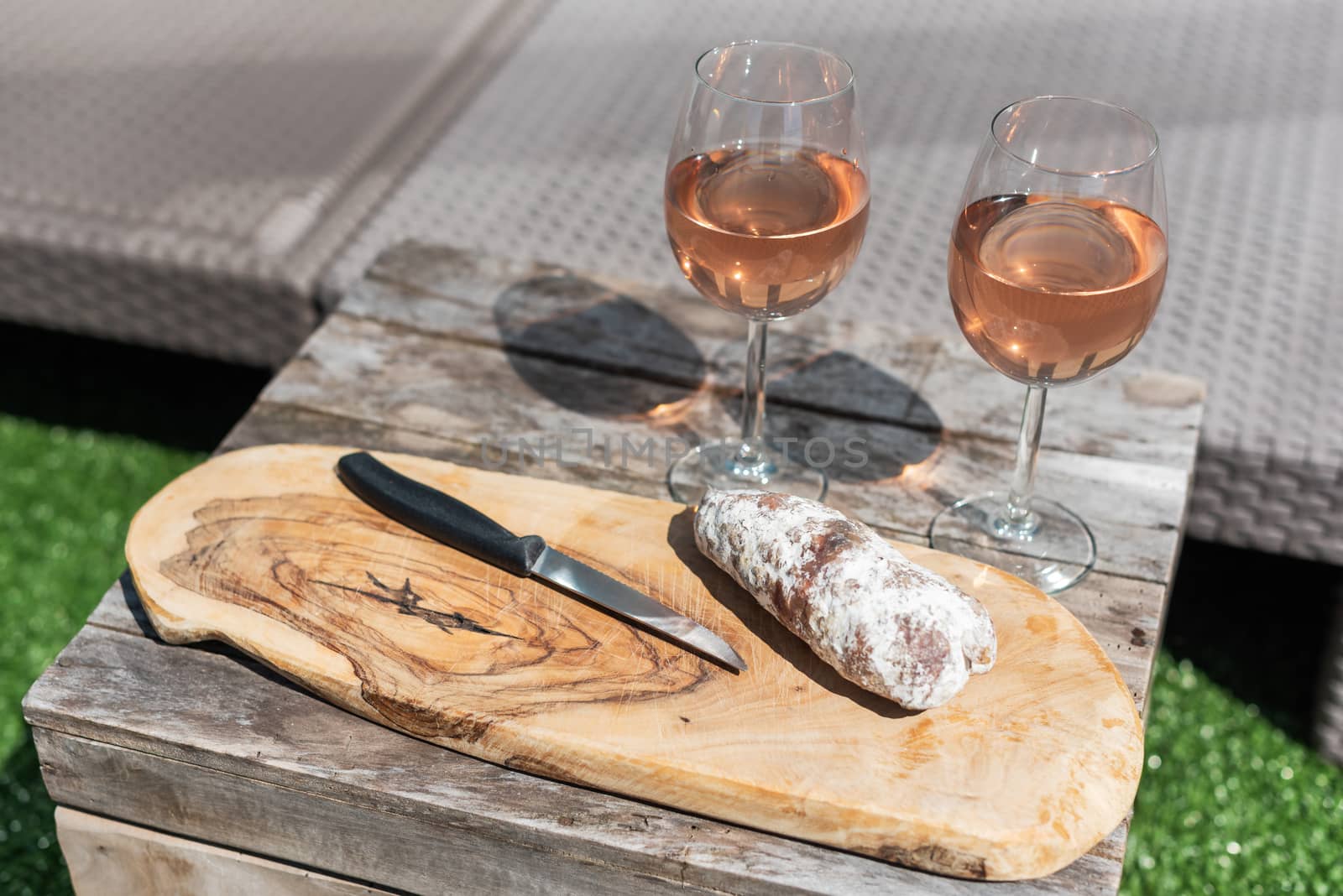 Two glasses of rose wine and a dried sausage with a knife on a wooden table by LP2Studio