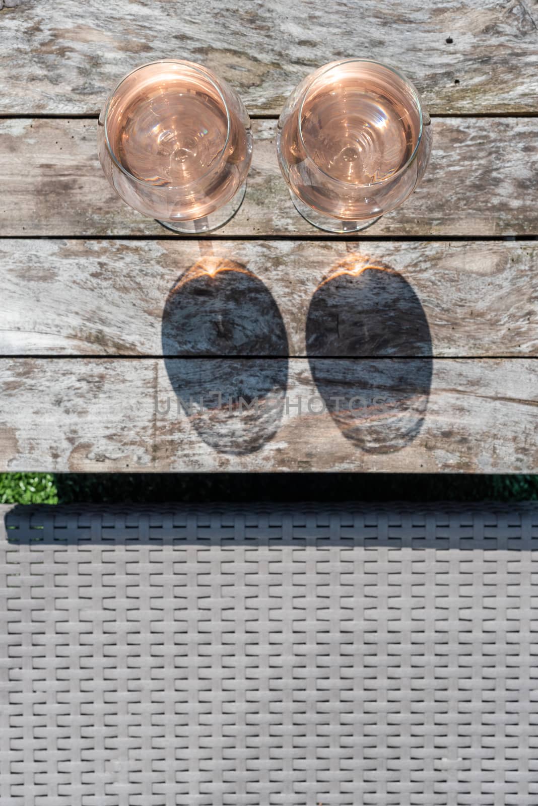 Two glasses of rose wine on a wooden table in sunlight top view