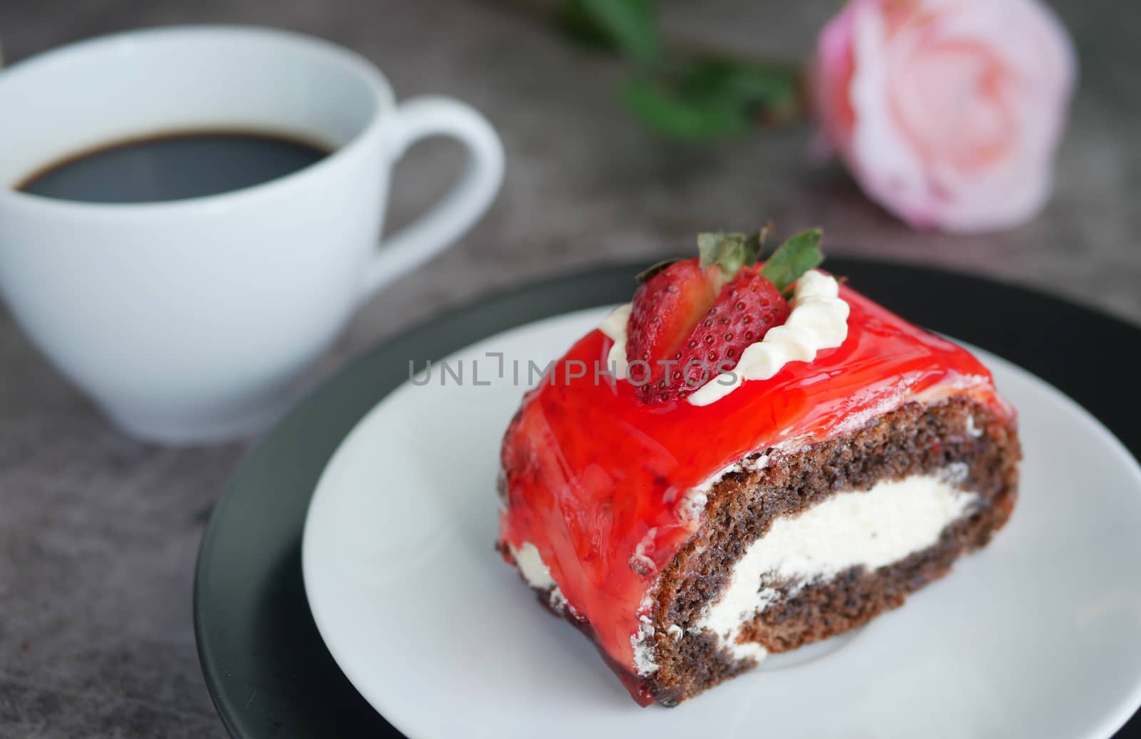 chocolate cake with strawberry jam sauce topped with whipped cream and fresh strawberry chopped served on white plate with a cup of black coffee, blur rose at background