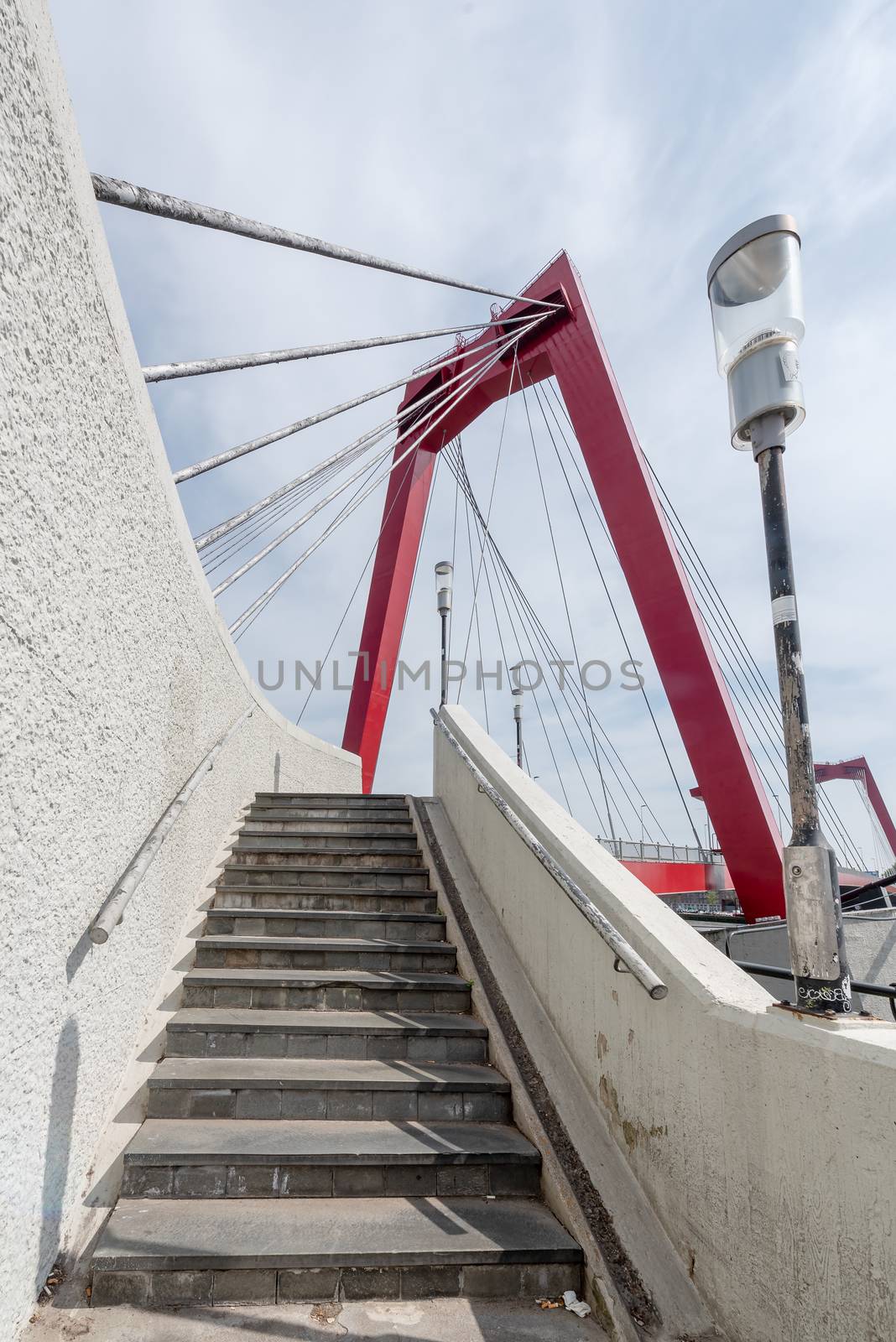 Willemsbrug bridge red cable bridge against blue sky and white clouds and with staircase in the foreground, Rotterdam, Netherlands