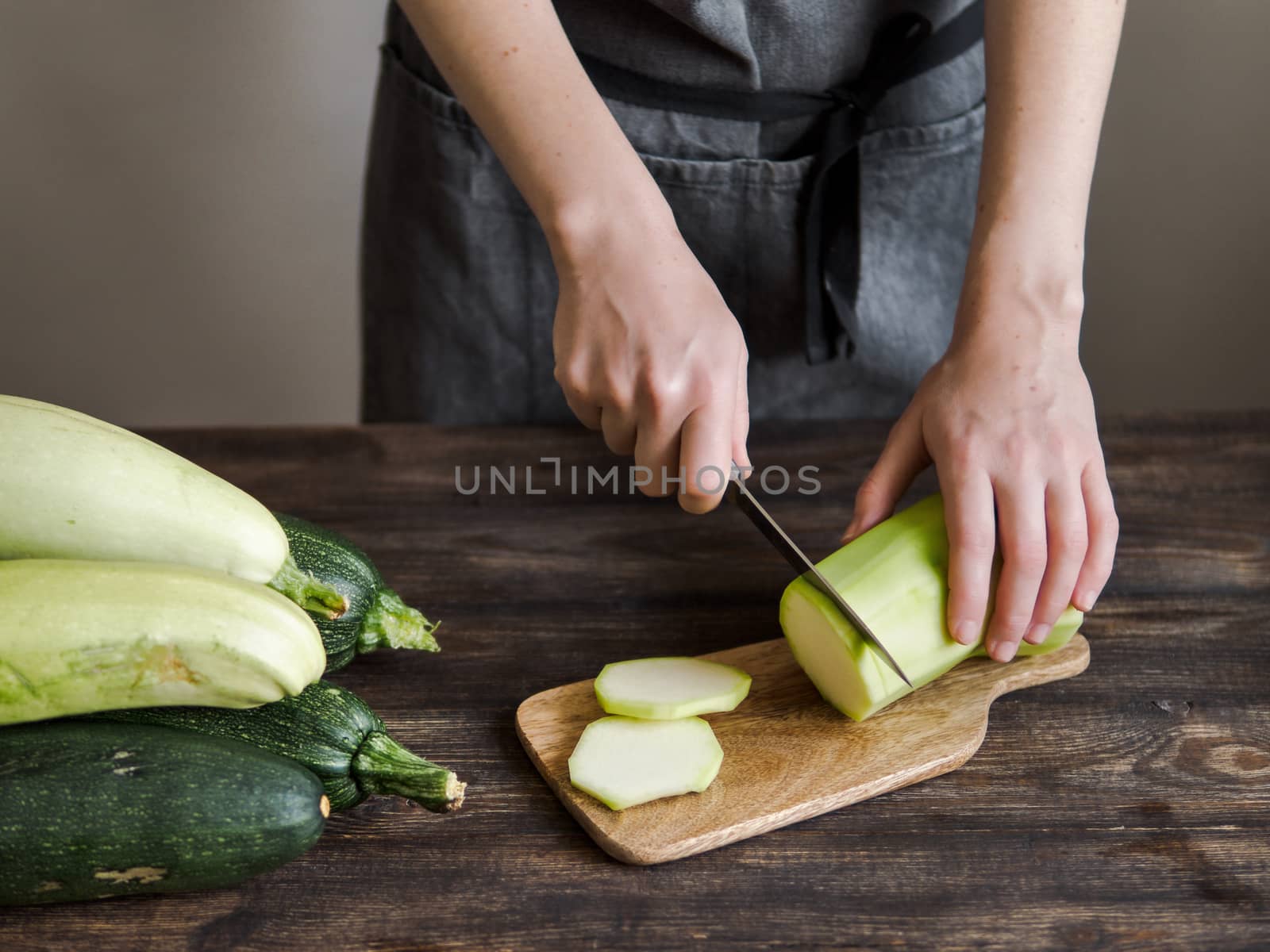 Zucchini harvest. Woman slices zucchini on wooden table. Farm organic zucchini harvesting
