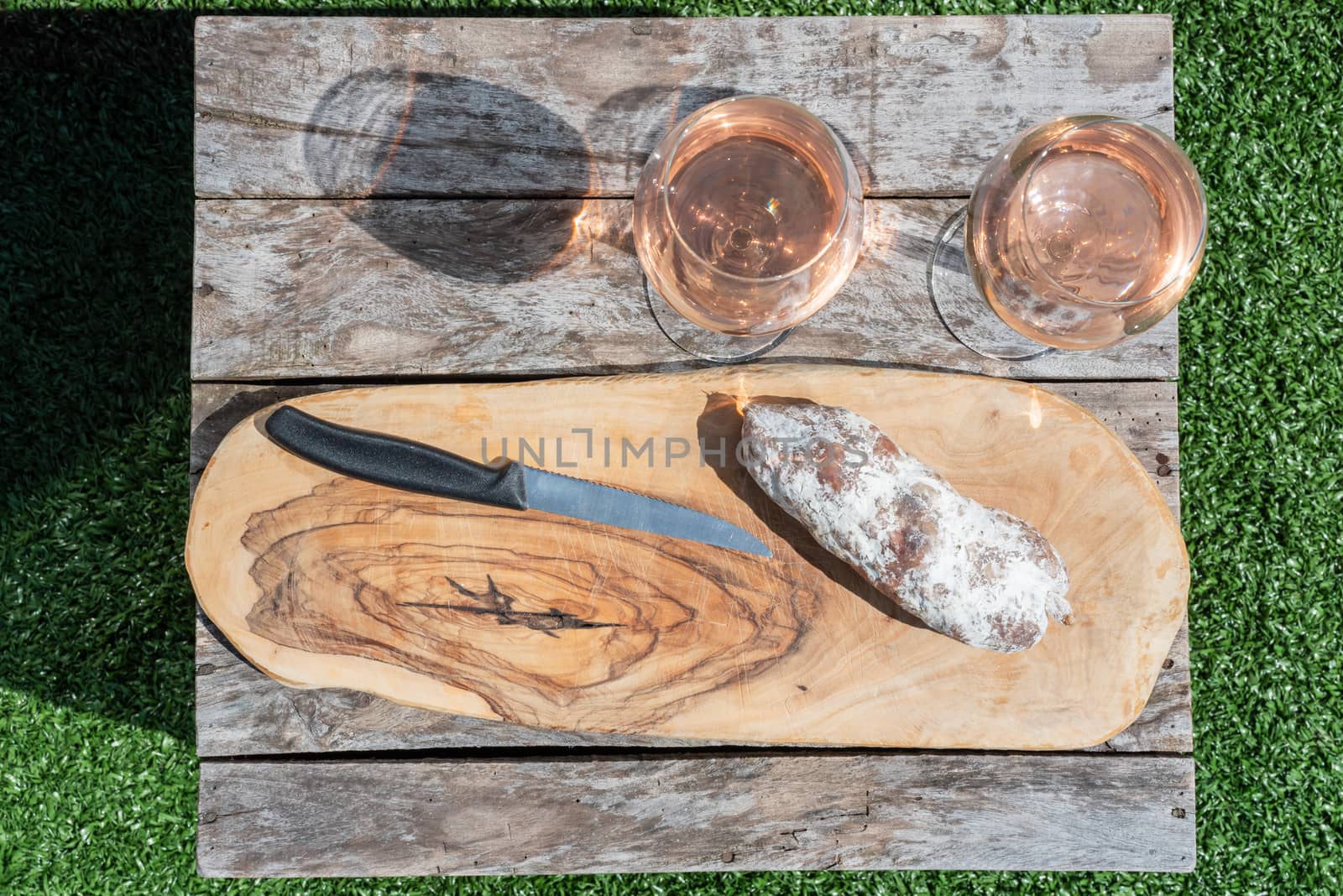Two glasses of rose wine and a dried sausage with a knife on a wooden table by LP2Studio