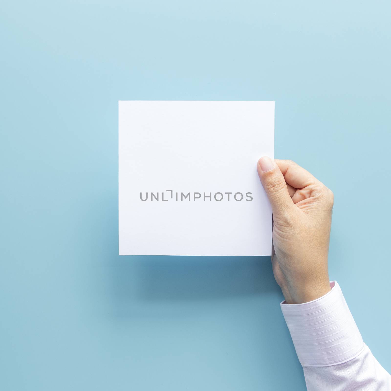 woman hand holding blank paper sheet isolated on blue background with copy space.