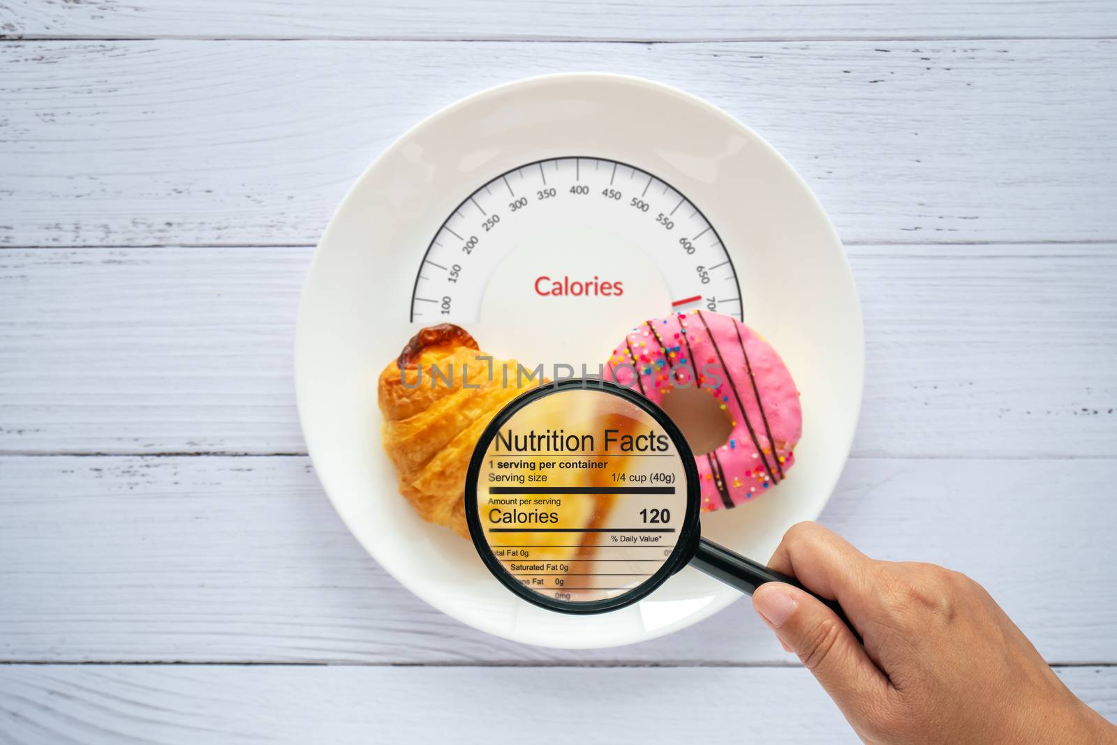 Calories counting, food control and consumer nutrition facts label concept. doughnut and croissant on white plate with tongue scales for Calories measuring and magnifying glass zoom for nutrition fact by asiandelight