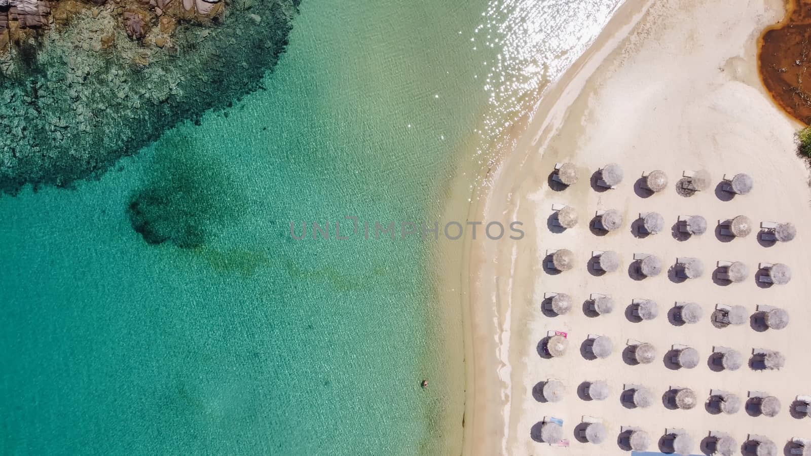 Aerial day top view of Sithonia Chalkidiki peninsula with crystal clear waters & sea beds with umbrellas next to small rocky island.