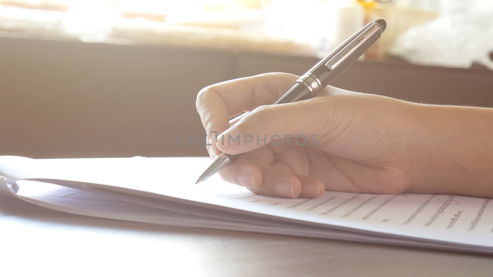 close up of woman hands signing or writing a document on a sheet of white paper with black pen in the morning