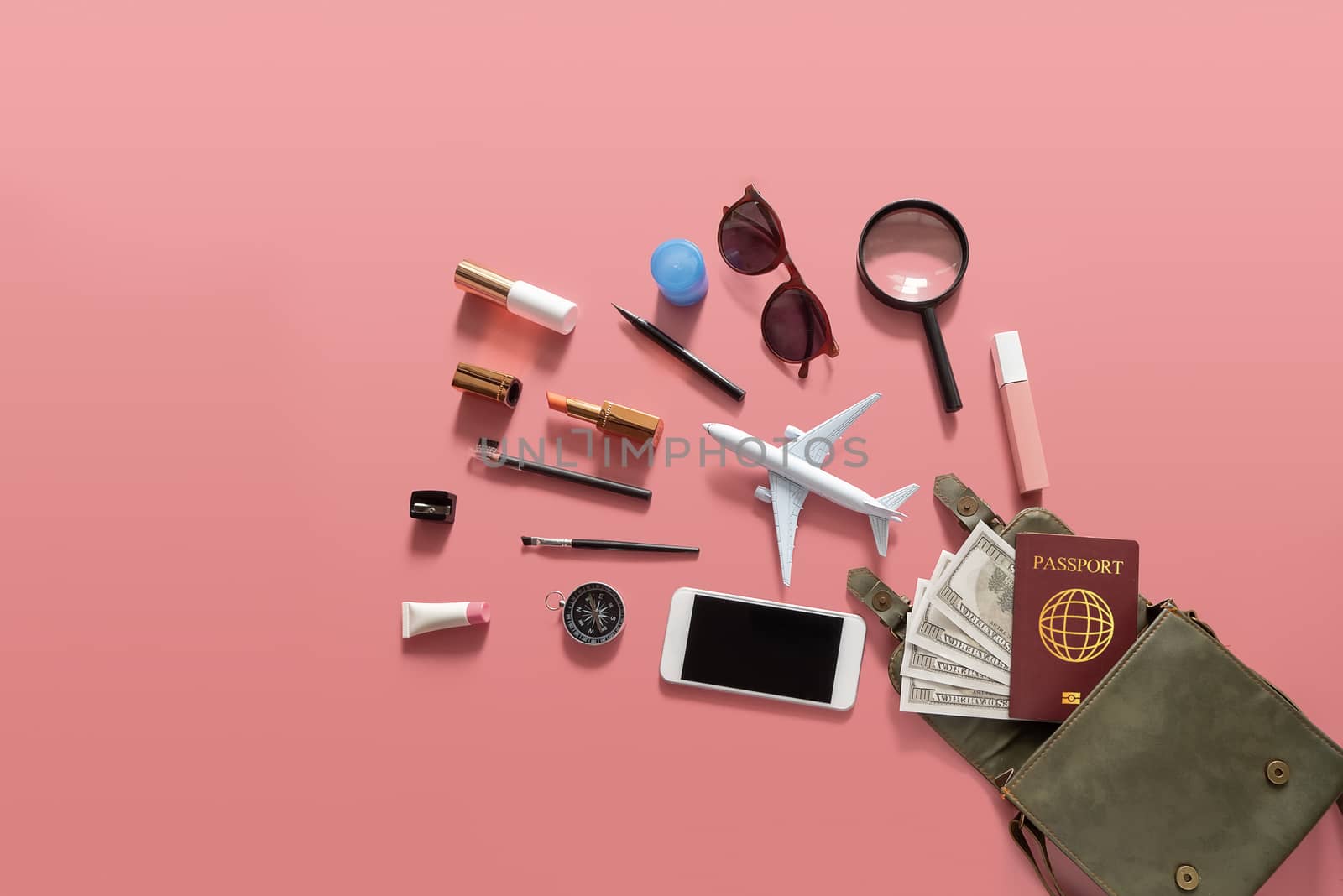 Flat lay of green leather woman shoulder bag open out with cosmetics, accessories , smartphone , money and passport on pink background