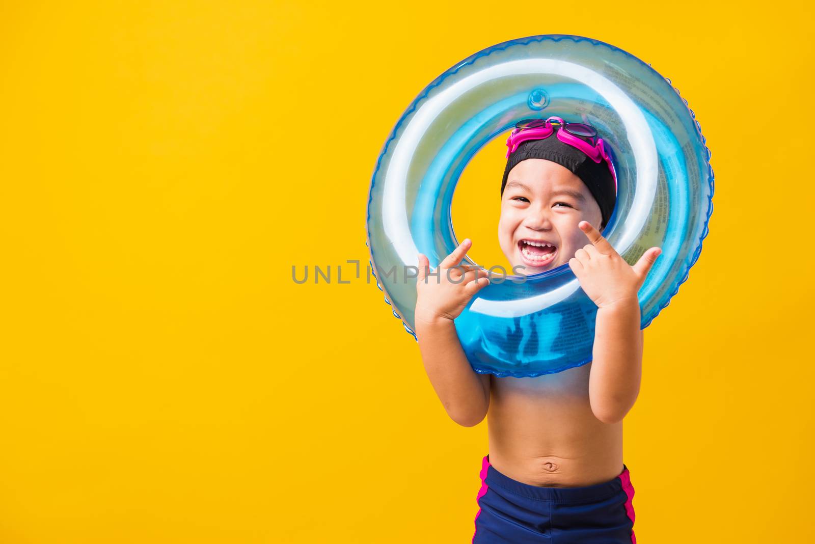 Summer vacation concept, Portrait Asian happy cute little child boy wear goggles and swimsuit hold blue inflatable ring, Kid having fun on summer vacation, studio shot isolated yellow background