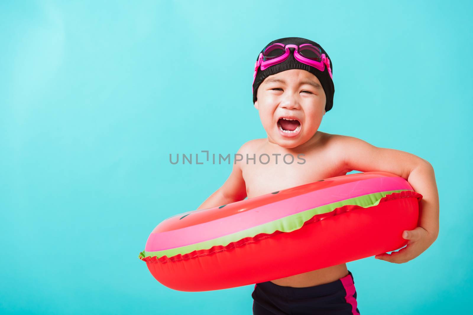 Summer vacation concept, Portrait Asian happy cute little child boy wear goggles and swimsuit hold watermelon inflatable ring, Kid having fun on summer vacation, studio shot isolated blue background