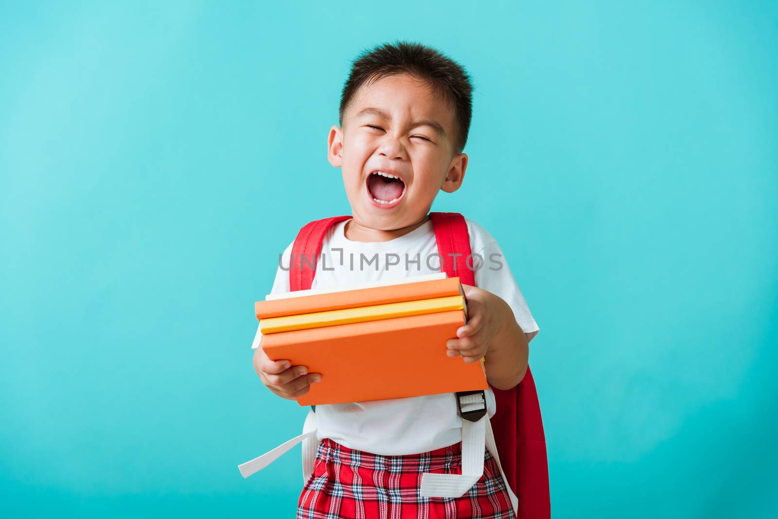 Back to school. Portrait Asian happy funny cute little child boy smiling and laugh holding books, studio shot isolated blue background. Kid from preschool kindergarten with school bag education