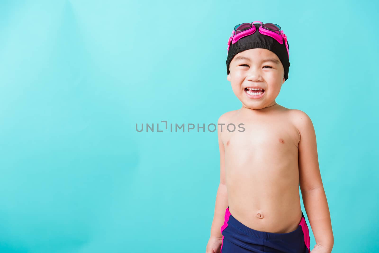 Summer vacation concept, Closeup portrait Asian happy cute little child boy wearing goggles and swimsuit, Kid having fun with in summer vacation looking camera, studio shot isolated blue background