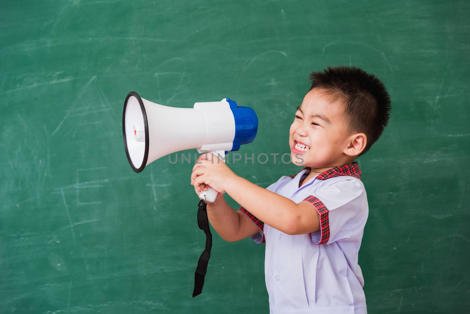 Back to School. Asian funny cute little child boy kindergarten preschool in student uniform speaking through megaphone against on green school blackboard, First time to school education concept