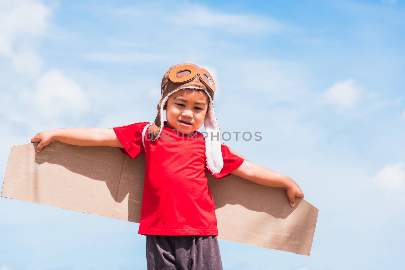 Happy Asian funny child or kid little boy smile wear pilot hat play and goggles with toy cardboard airplane wing flying outdoor against summer blue sky cloud background, Startup freedom concept