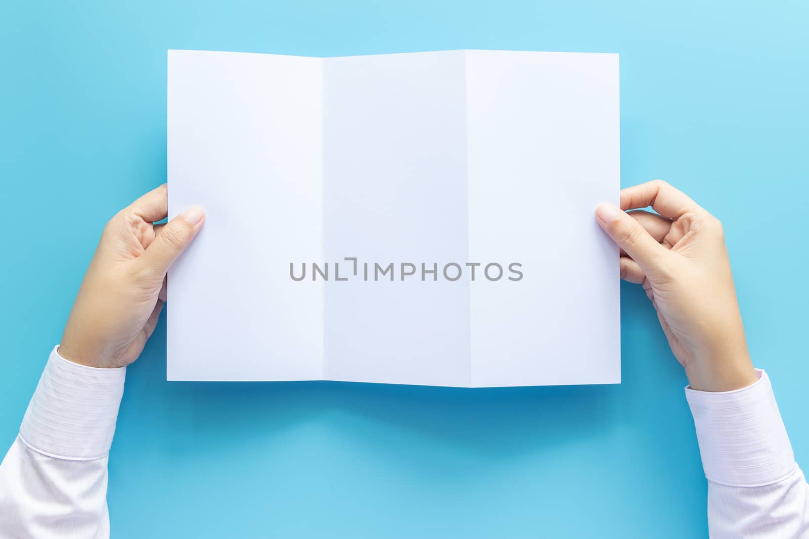 hand holding blank white paper for letter mock up, isolated on blue background with copy space. studio shot, horizontal by asiandelight