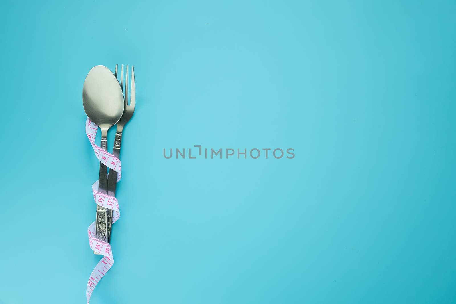 spoon and fork wrapped in measuring tape isolated on blue background with copy space. diet , food control and weight loss concept.