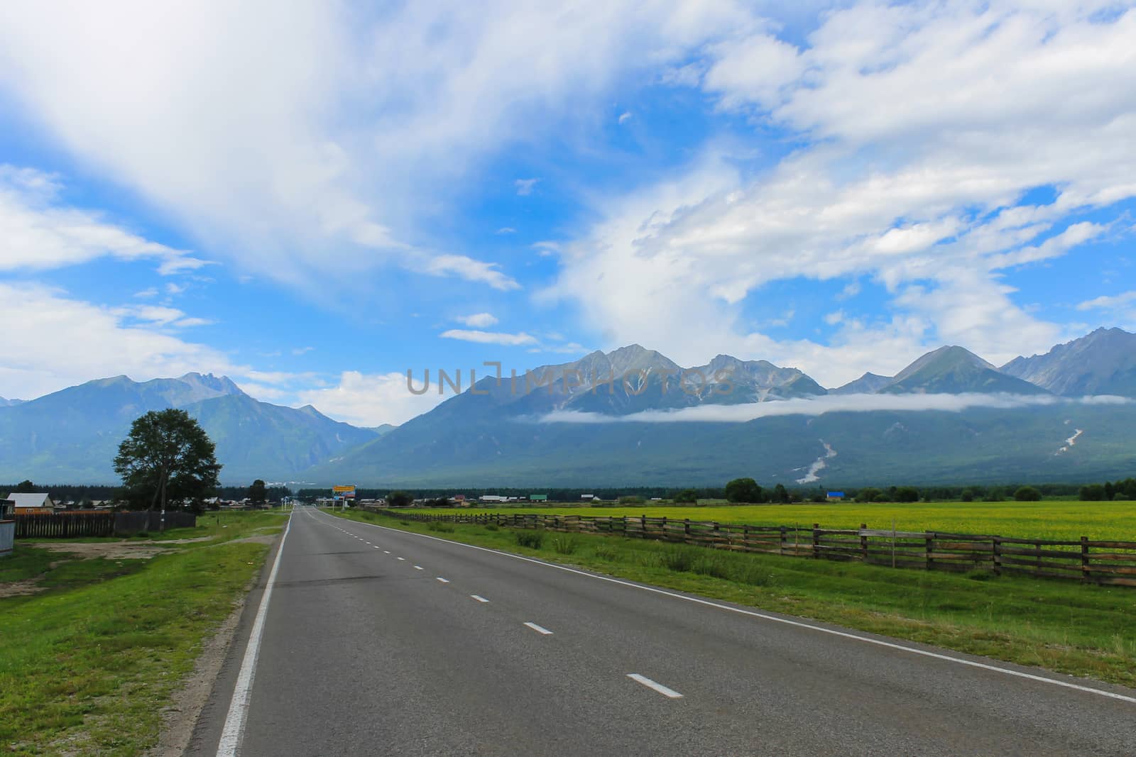 The road leading to the foot of the mountains past the green field by Skaron