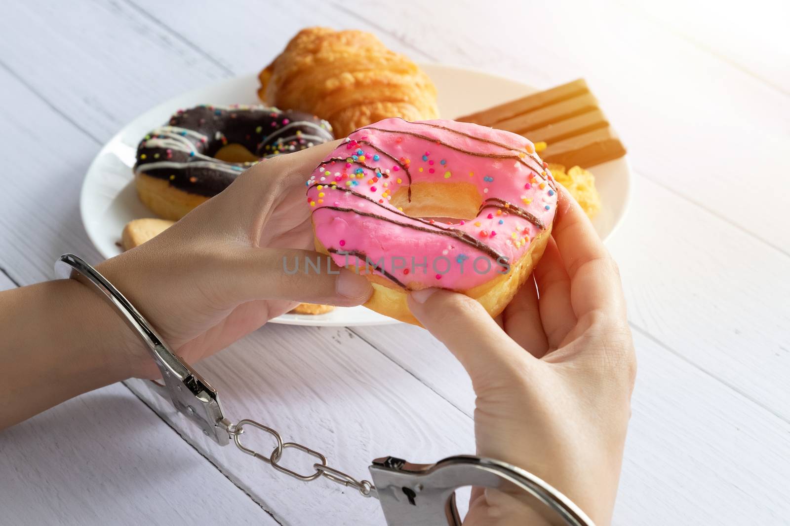 Calories control, food diet and weight loss concept. top view of two hands was control by handcuff, holding doughnut from white dish on dining table