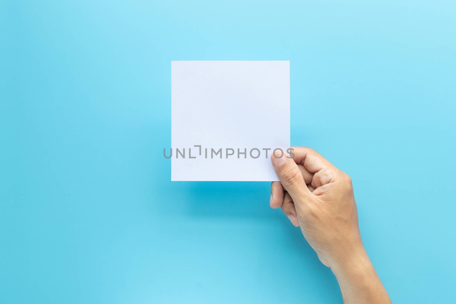 man hand holding blank card paper sheet isolated on blue background with copy space.