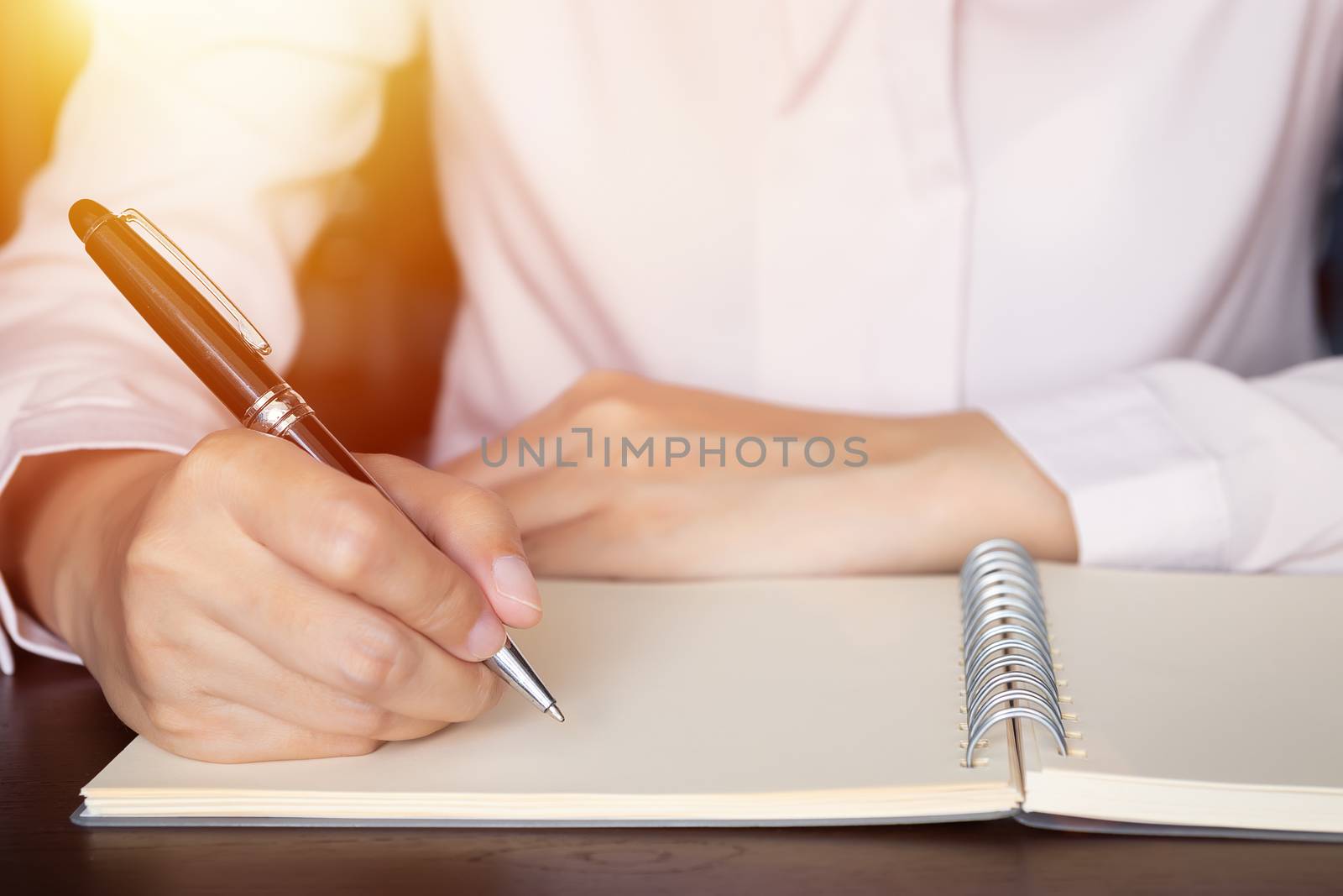 close up of business woman hands writing in spiral notepad on wooden table by asiandelight