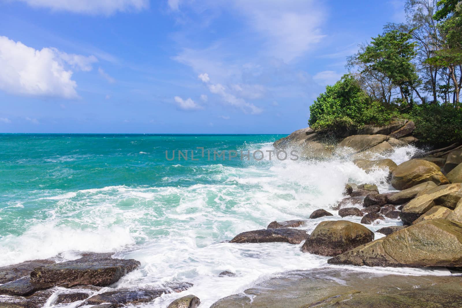 Waves hit rocks on the shore of the blue sea