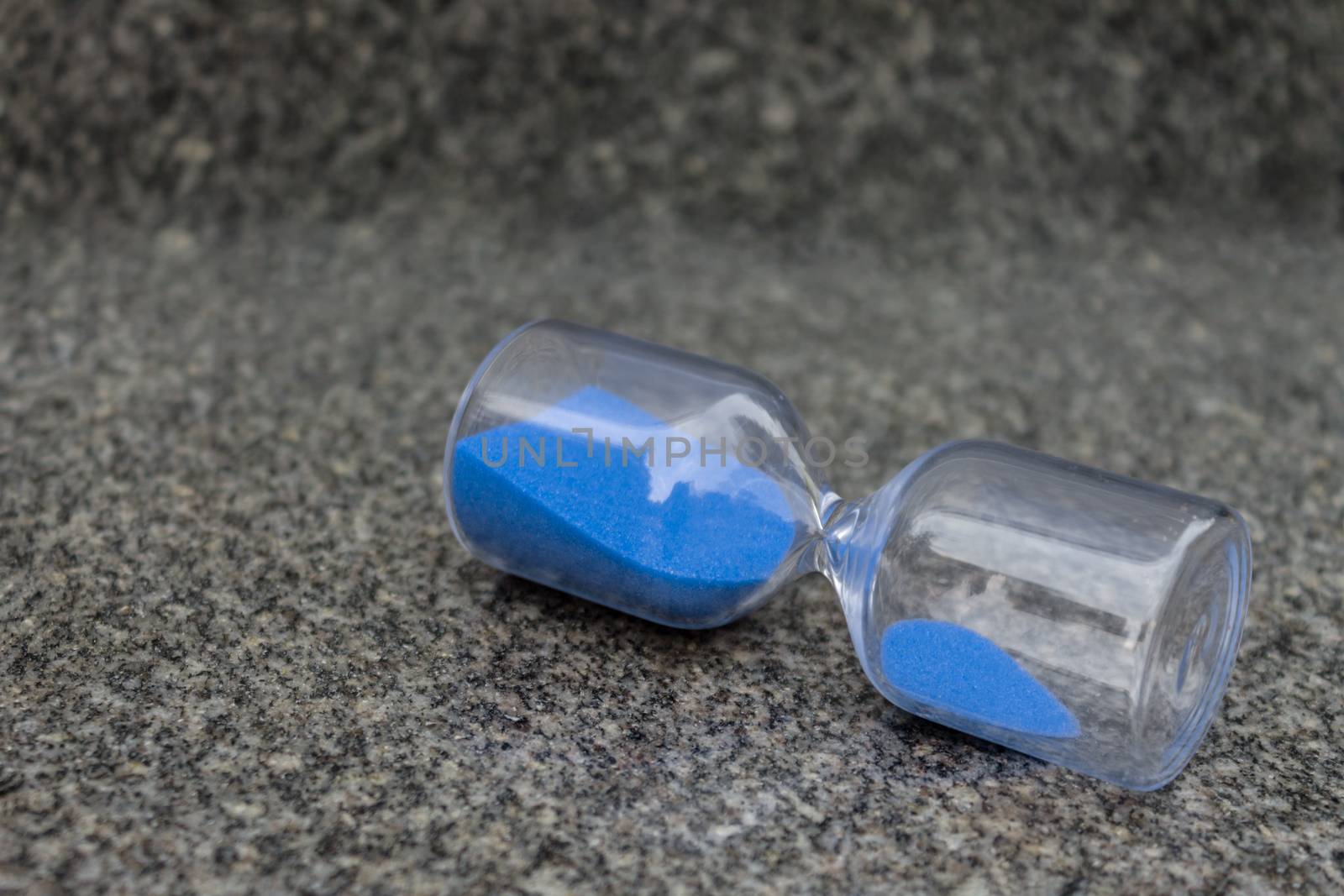 Glass hourglass with blue granules lie on gray granite