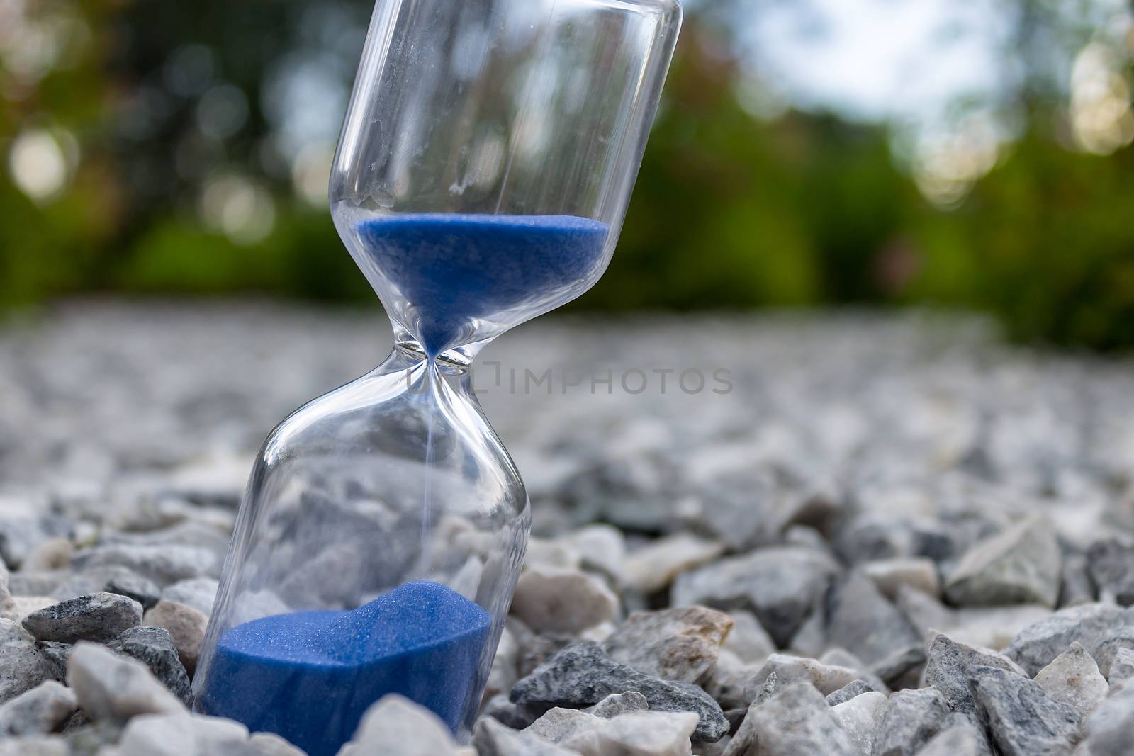 Hourglass with beautiful blue sand lie on small stones