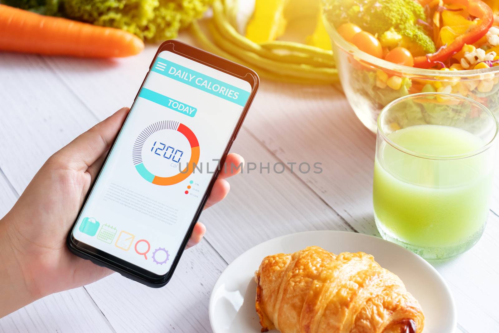Calories counting and food control concept. woman using Calorie counter application on her smartphone with salad , vegetable, juice and croissant on dining table by asiandelight