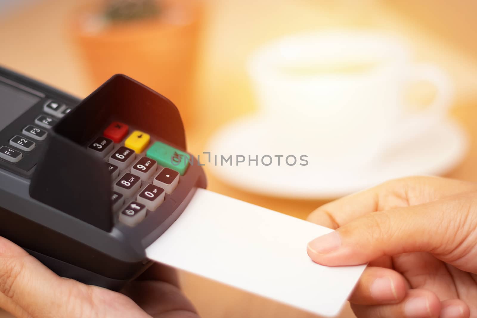 credit card payment concept. close-up hand insert credit card mock up with white blank card with a card swipe machine at point of sale terminal in coffee shop