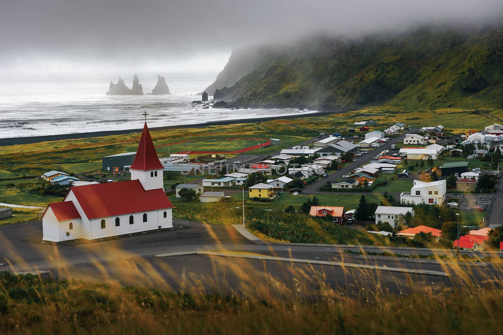 Heavy clouds over the village of Vik and its lutheran church in Iceland with Reynisdrangar basalt sea stacks in the background.