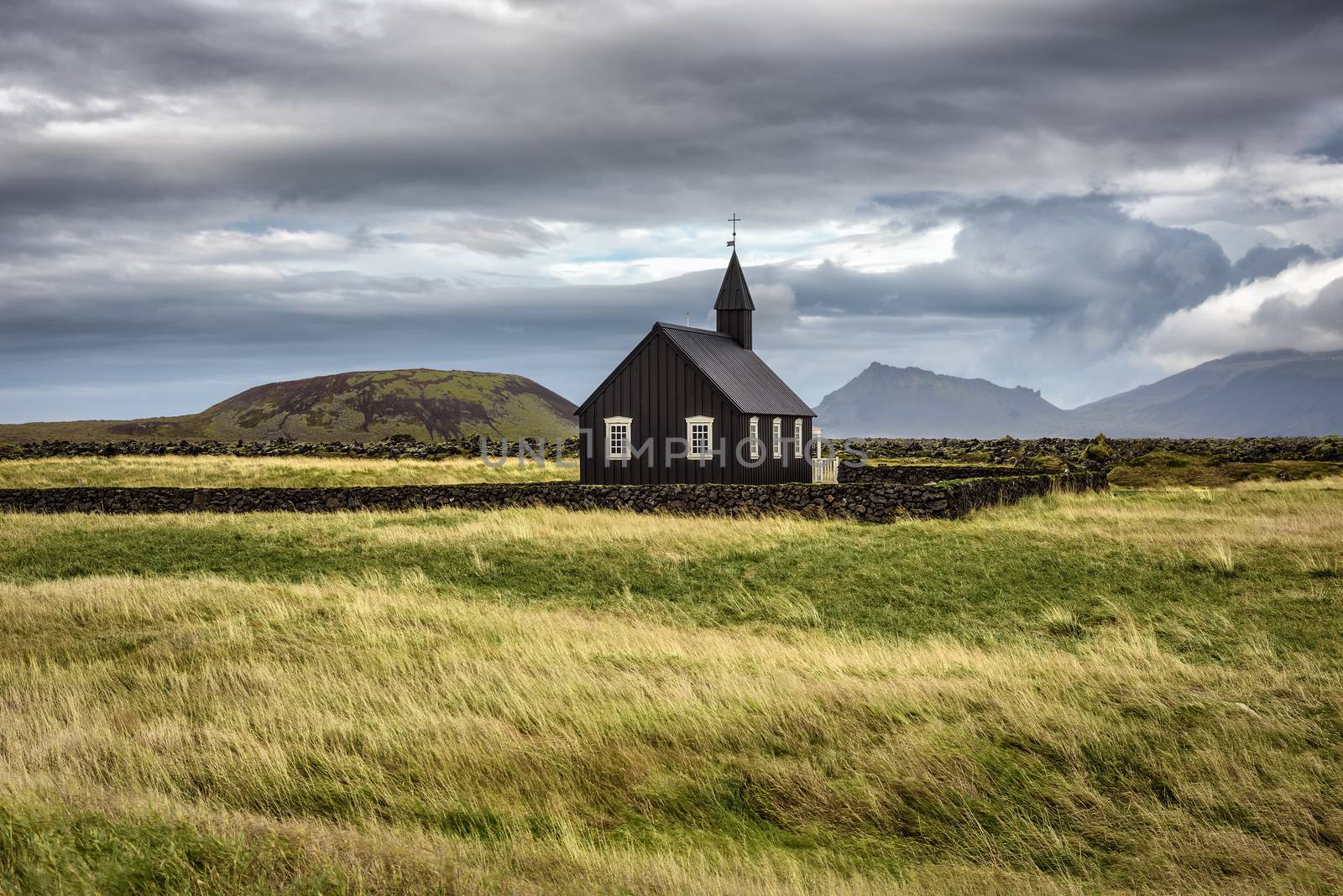 Scenery of black wooden church of Budir in Iceland with the pasture and mountains in the background