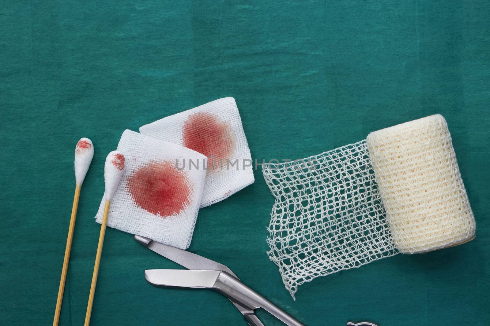 Gauze,blood,scissors,roll gauze and two swab cotton bus sticks on green medical surgical dress and copy space