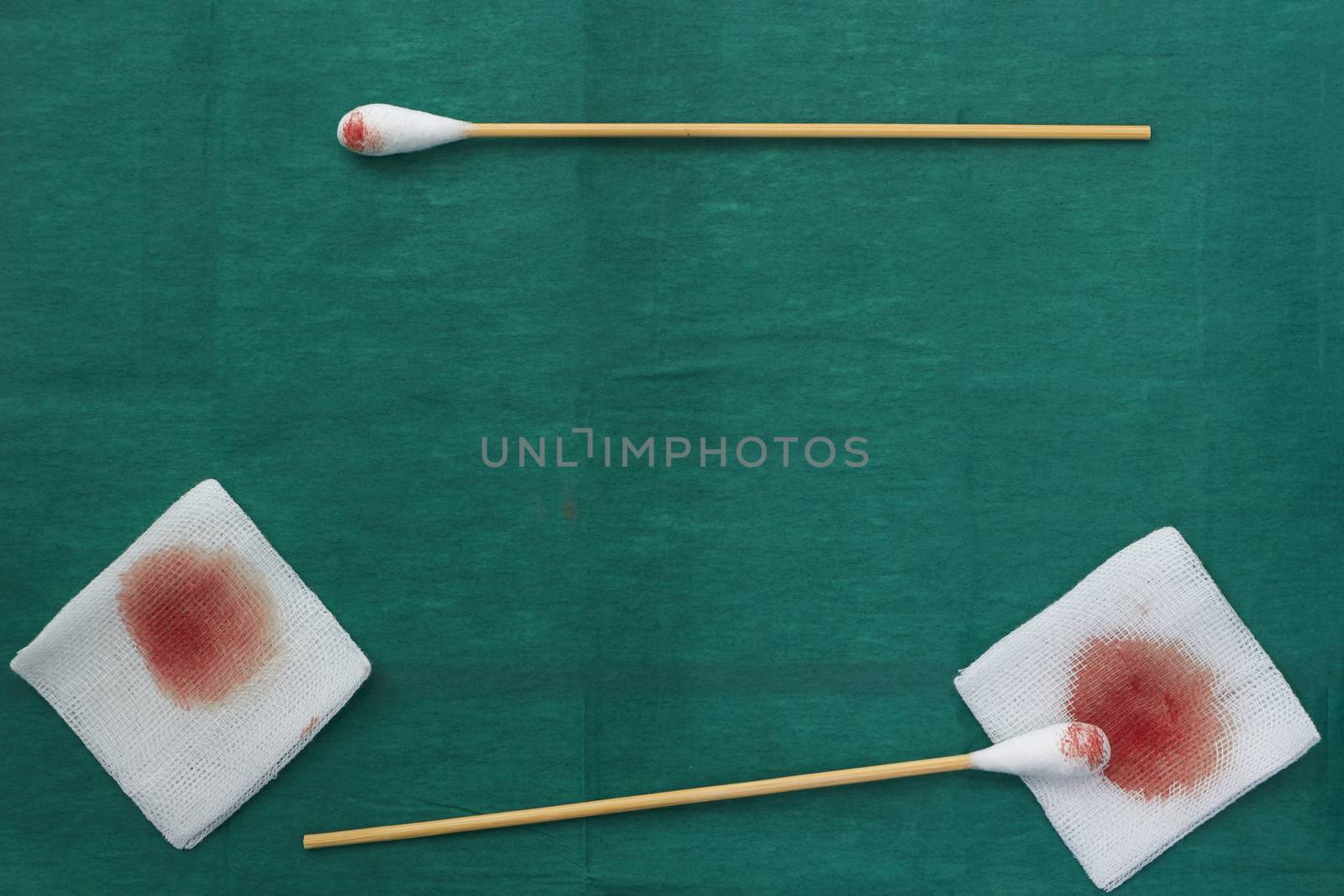 Gauze,blood,scissors and two swab cotton bus sticks on green medical surgical dress and copy space