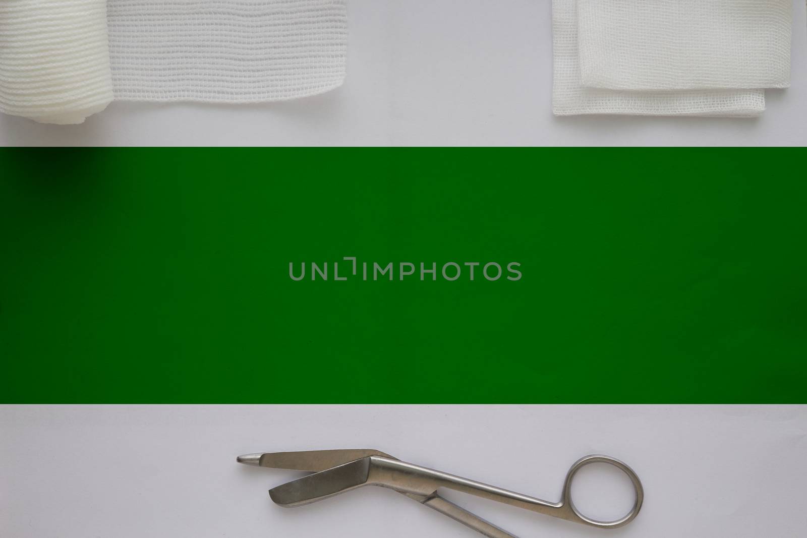 Gauzes, scissors and roll gauze on white background with green strip copy space