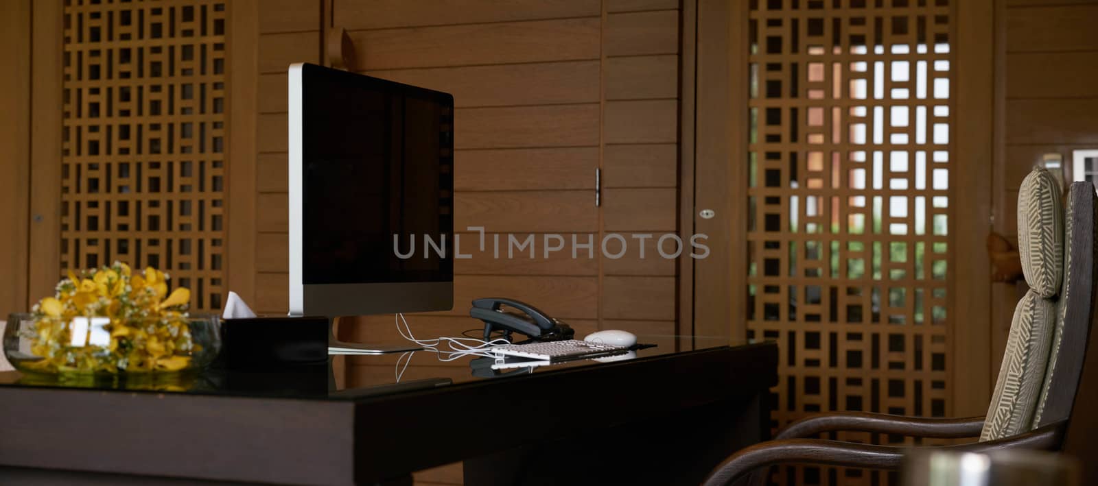 Working office table with computer desktop and telephone and armchair and vase