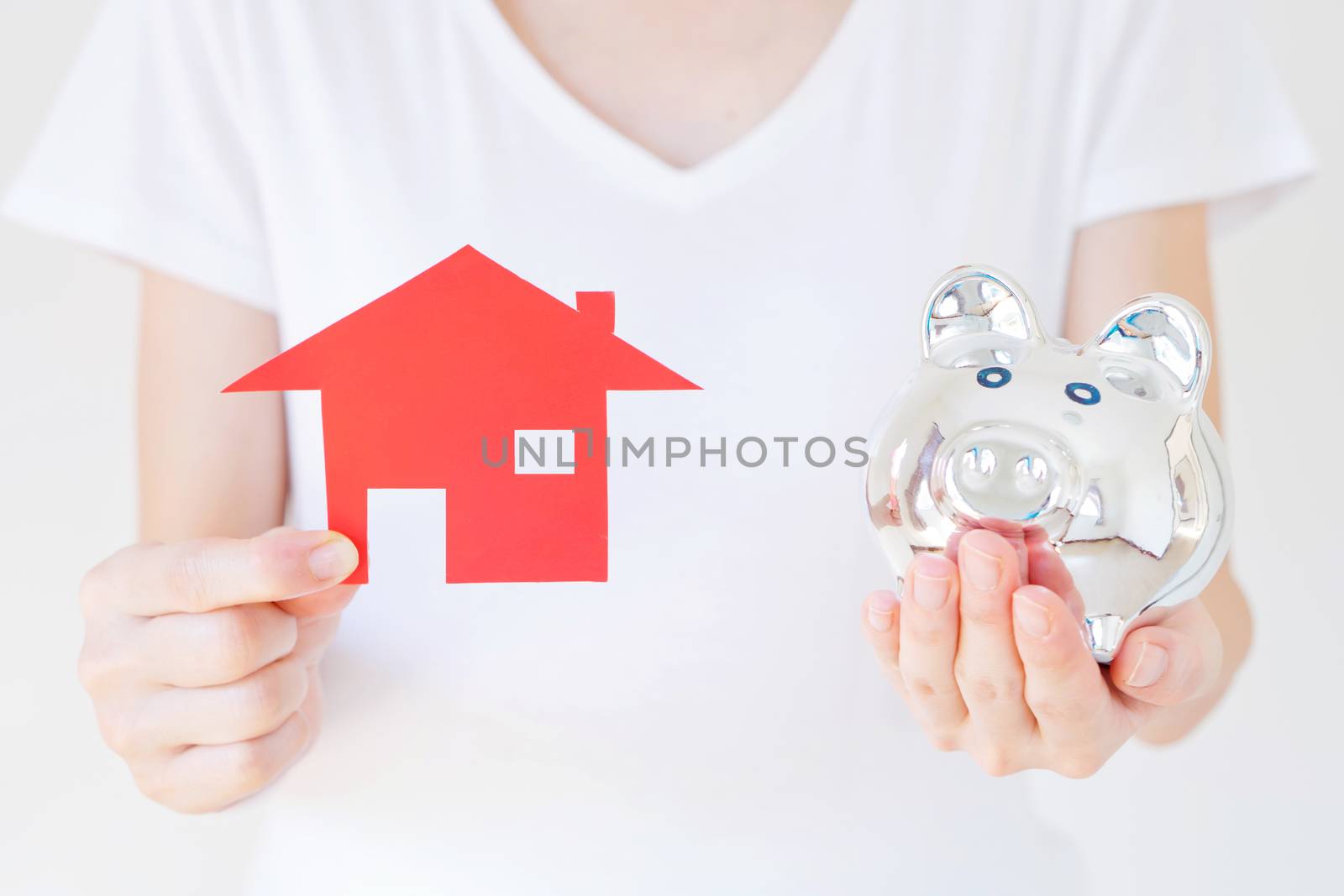 Hands holding a piggy bank and a house model.