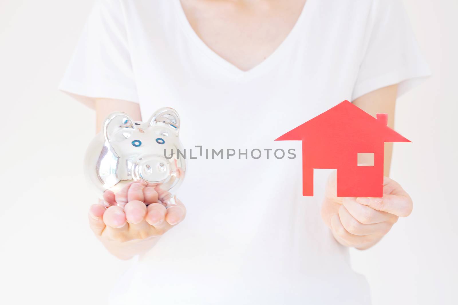 Hands holding a piggy bank and a house model.