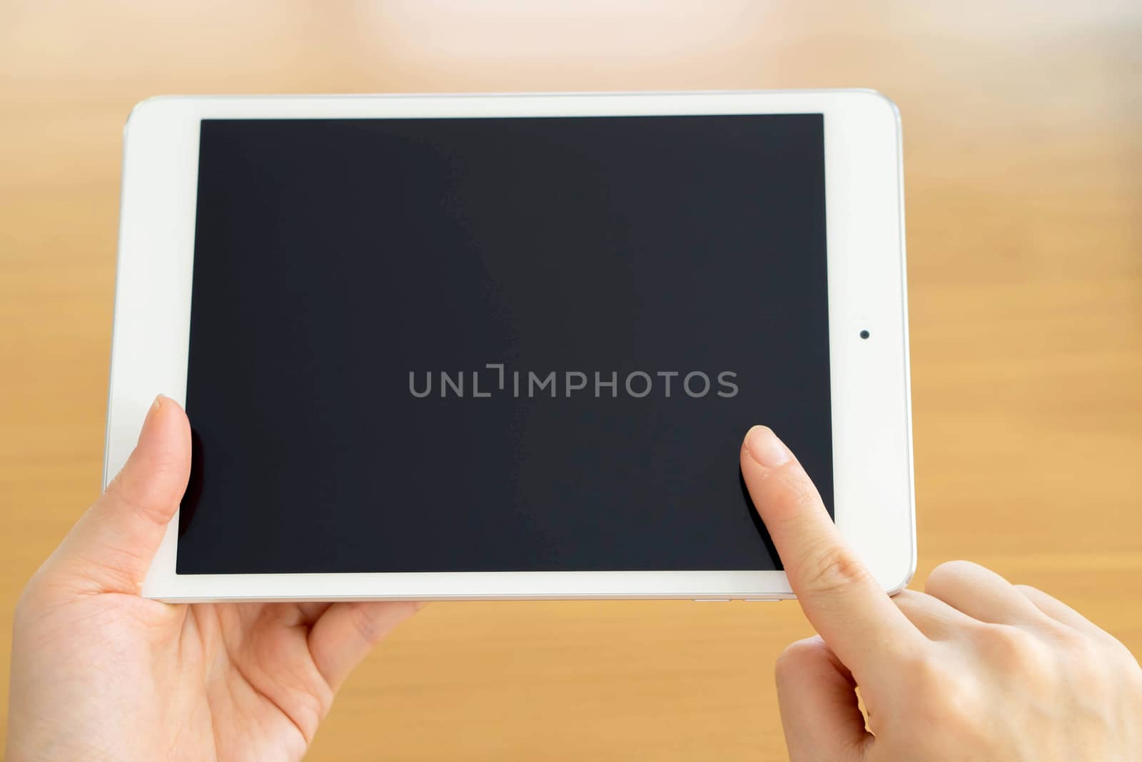 woman's hand holding a tablet on the background of a wooden tabletop