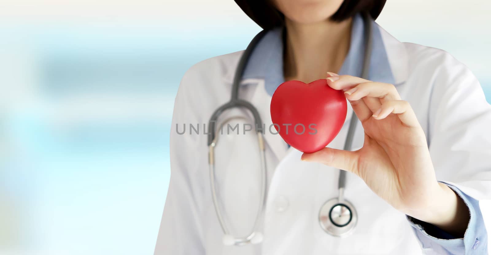 Positive female doctor standing with stethoscope and red heart symbol isolated