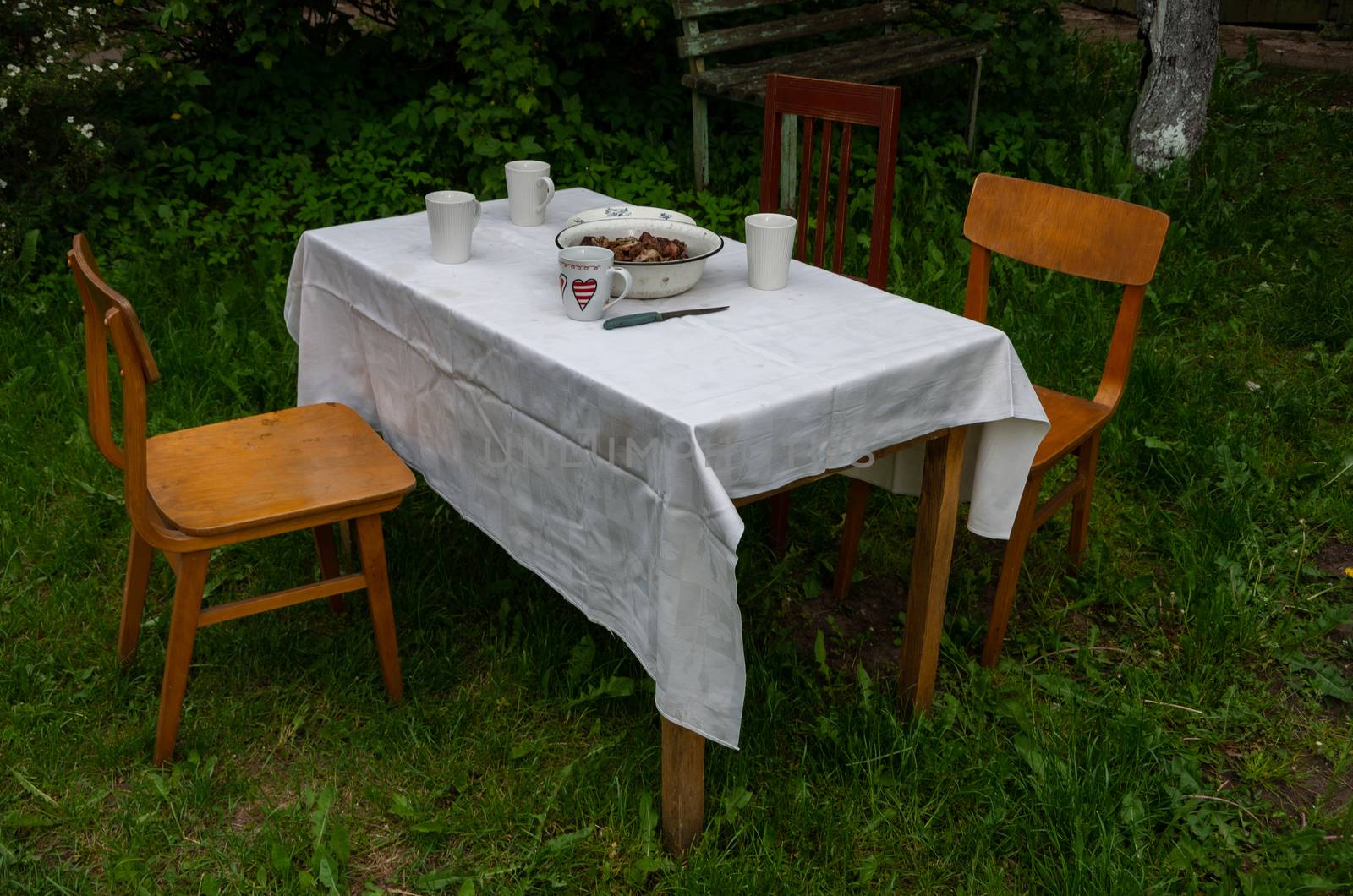Outside table with mugs and meat and old chairs, white