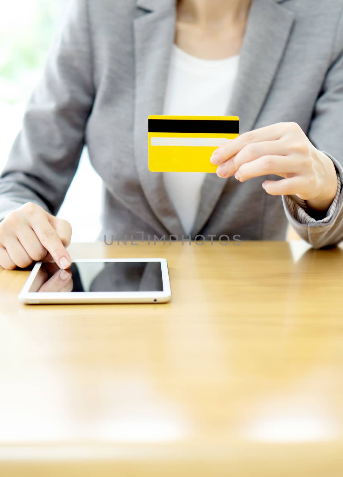 Close-up woman's hands holding a credit card and using tablet pc by ekachailo