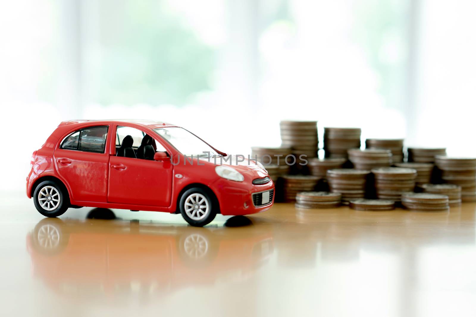 Stacks of giant silver coins next to a new red car 