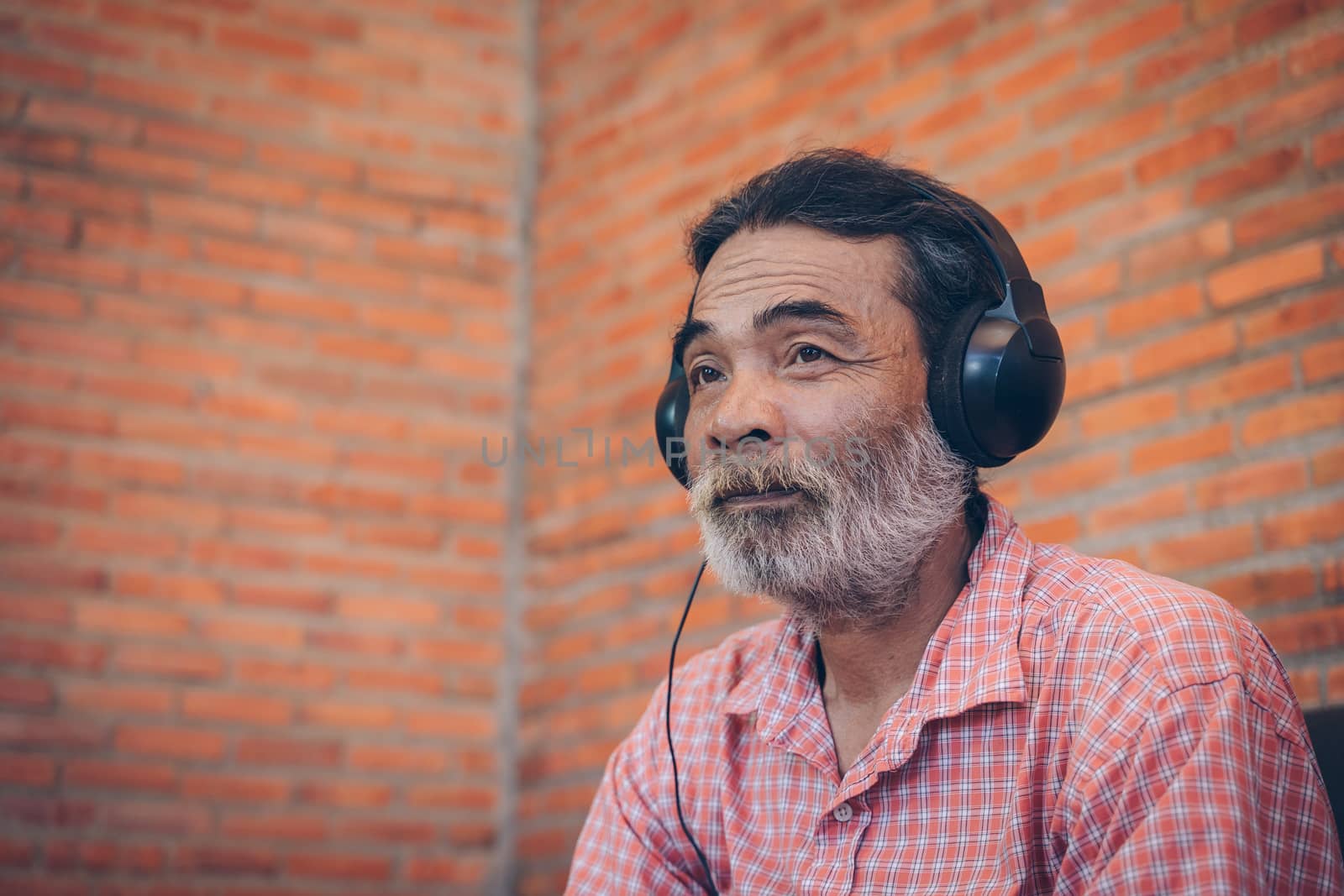 The old man listens to the music from the headphones. by Visoot