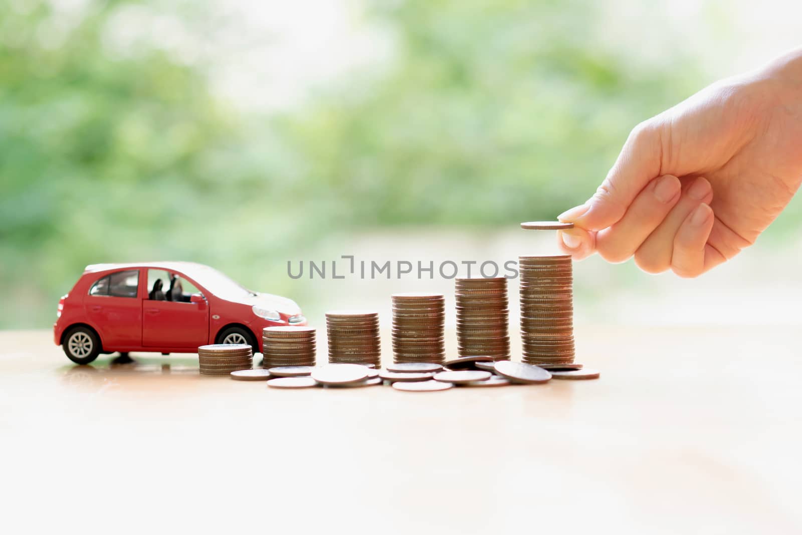 Businesswoman hand pushing a toy car over a stack of coins