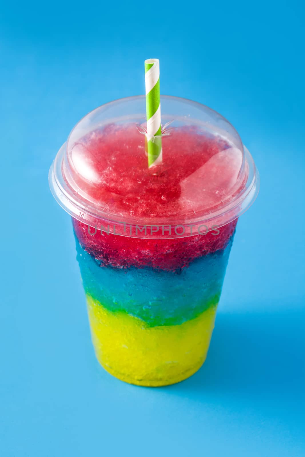 Colorful slushie of differents flavors with straw on blue background